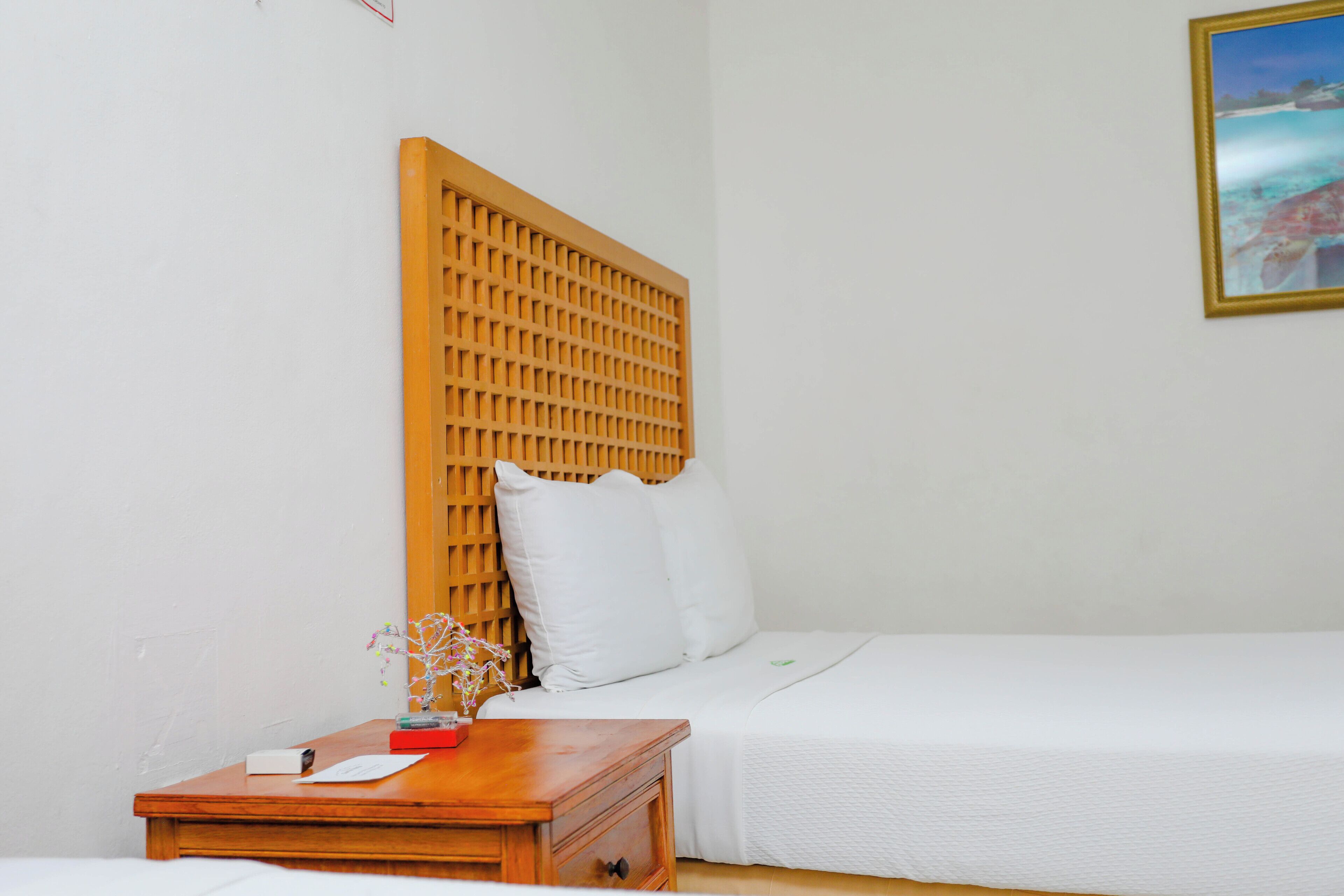 A bedroom with a wooden headboard, a bedside table with a book and a vase, and a bed with white bedding.