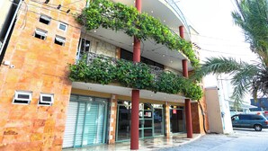 Un edificio de varios pisos con un balcón curvo, ventanas grandes y un pilar rojo.