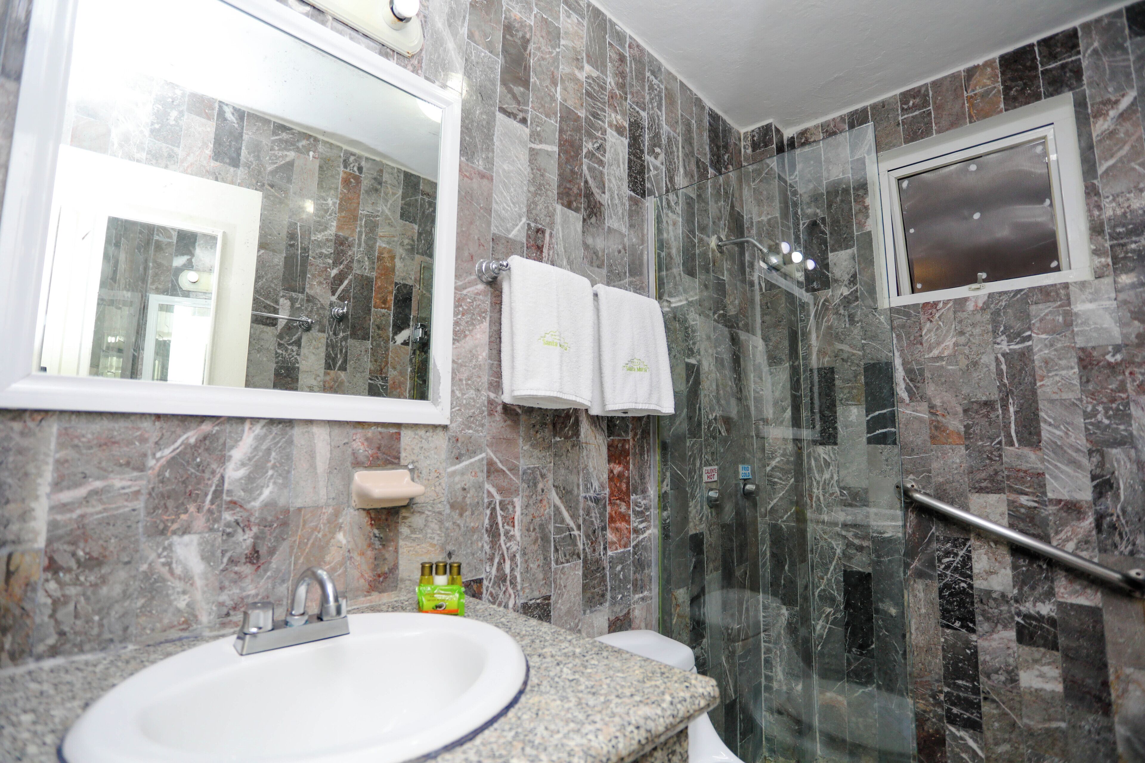 Un baño con pared de mármol, un lavabo, una cabina de ducha de vidrio y un espejo.