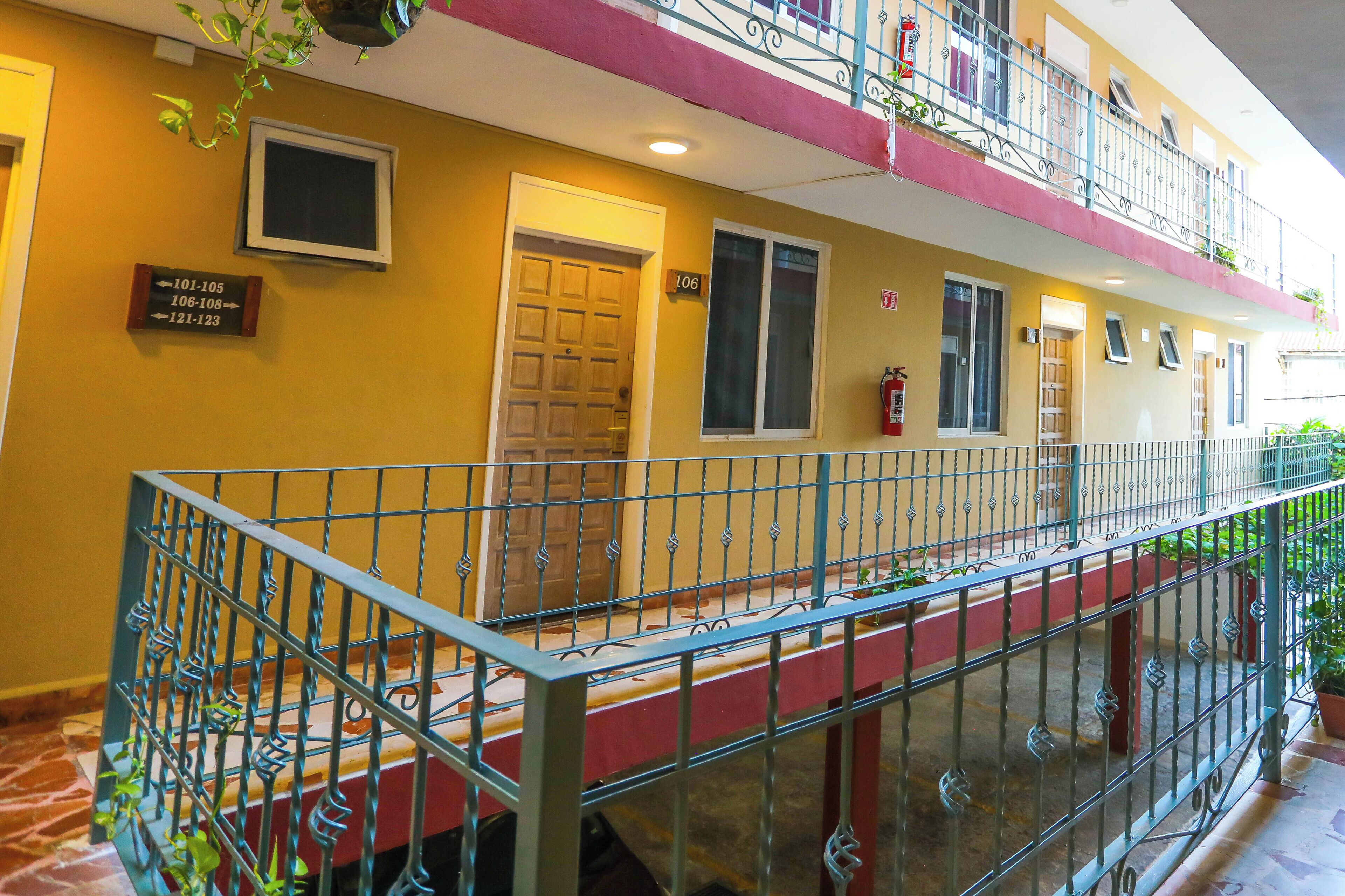 Hotel com fachada em vermelho e amarelo, varanda com grades de metal e portas numeradas indicando a atribuição dos quartos.