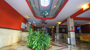 Un vestíbulo con una planta central, techo con tragaluces y una zona de recepción con televisor.