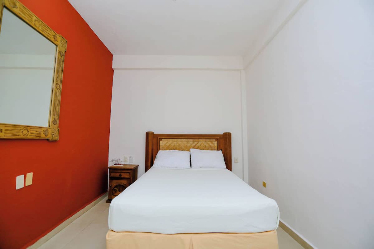 Un letto singolo con testiera in legno in una stanza dalle pareti rosse e modanature bianche.