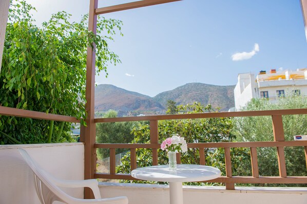 A balcony with a white table and chair, a vase of flowers, and a view of mountains and greenery.