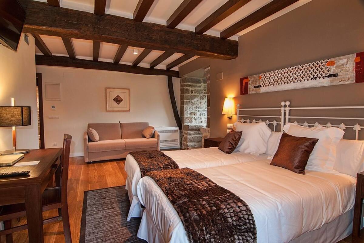 A bedroom with a large bed, a sofa, a desk, and a stone wall.