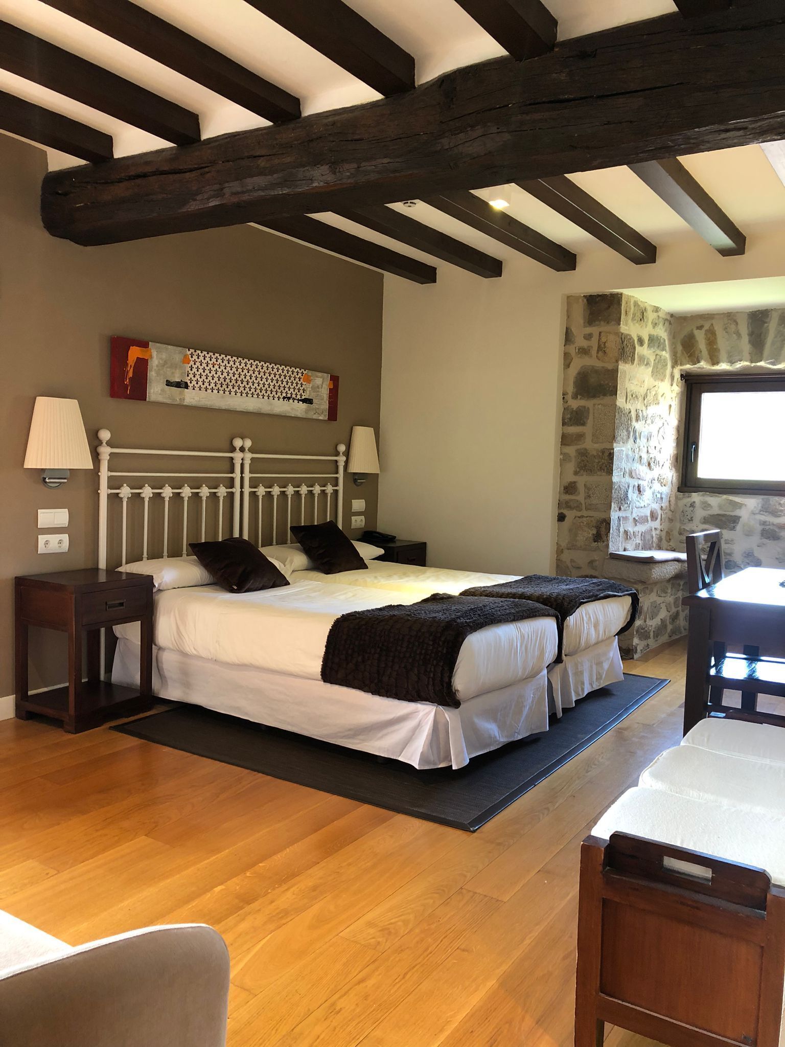 Un dormitorio con dos camas, vigas de madera, una pared de piedra y una ventana.