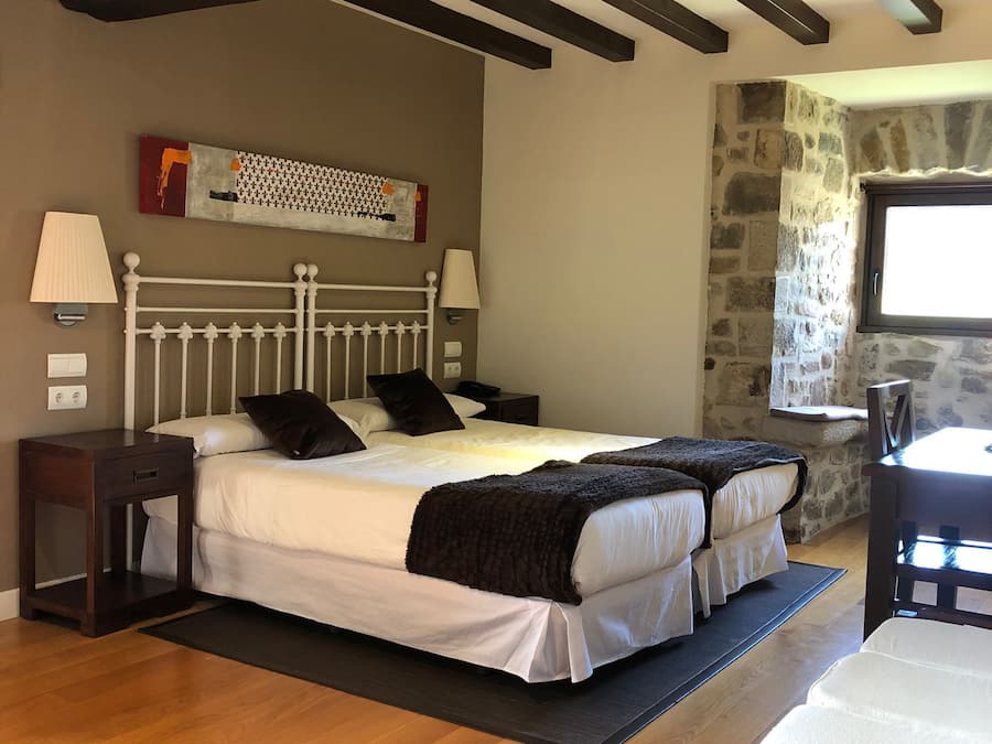 Una camera da letto con due letti, travi in legno, una parete in pietra e una finestra.