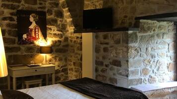 A bedroom with a stone wall, a bed with white bedding, a bedside table with a lamp, and a poster on the wall.