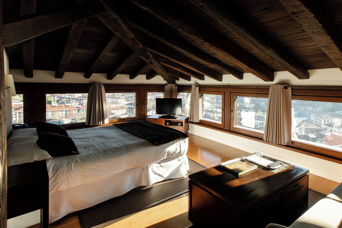 A bedroom with a large bed, a TV, and a view of the city through large windows.