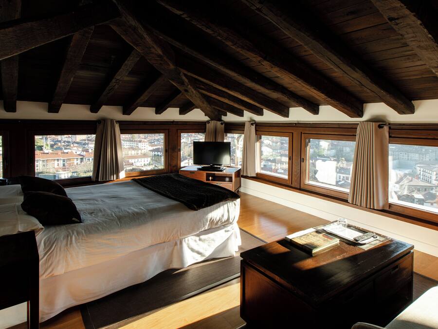 Un dormitorio con una cama grande, televisión y vistas de la ciudad a través de amplios ventanales.