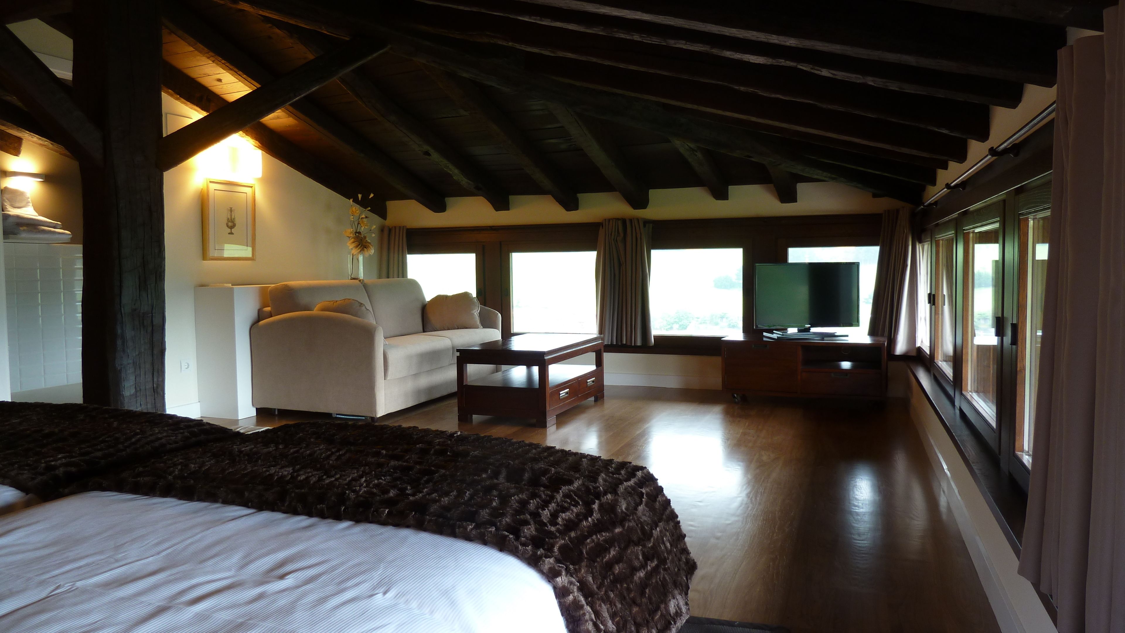 Une chambre d’hôtel avec un lit, un canapé, une télévision et une table basse en bois.