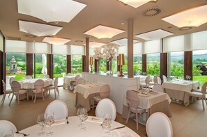 A dining area with multiple tables and chairs, large windows offering a view of greenery and a distant building. - Hotel Torre Zumeltzegi (Oñati)