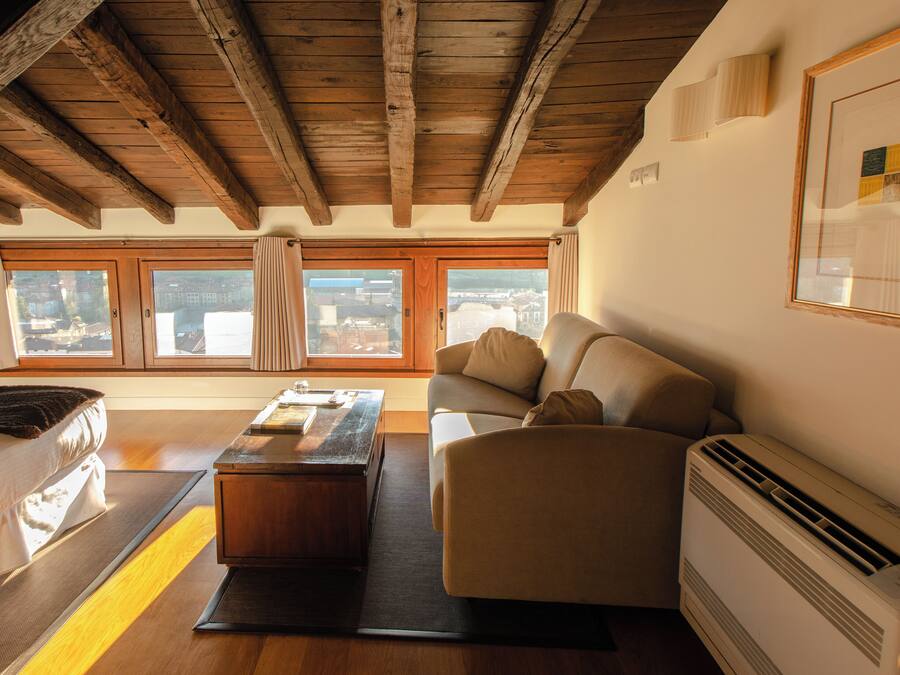 A cozy living room with a wooden ceiling, a sofa, a coffee table, and a view through large windows.