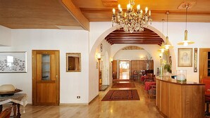Un vestíbulo de hotel con un mostrador de recepción de madera, una araña y una alfombra roja que conduce a un comedor.