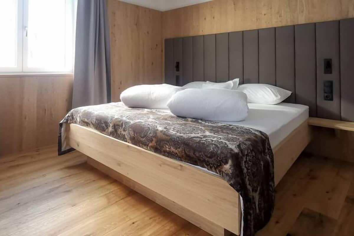 A modern bedroom with a wooden headboard, a bed with white bedding, and a window with curtains.