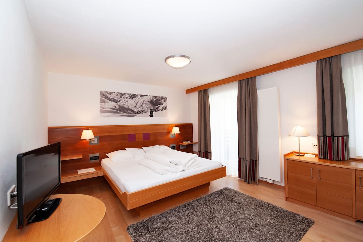 A hotel room with a bed, a TV, a desk, and a large window with curtains.