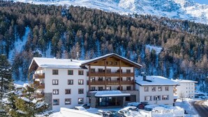 Un hotel de varios pisos con tejado nevado, rodeado de un bosque y montañas.