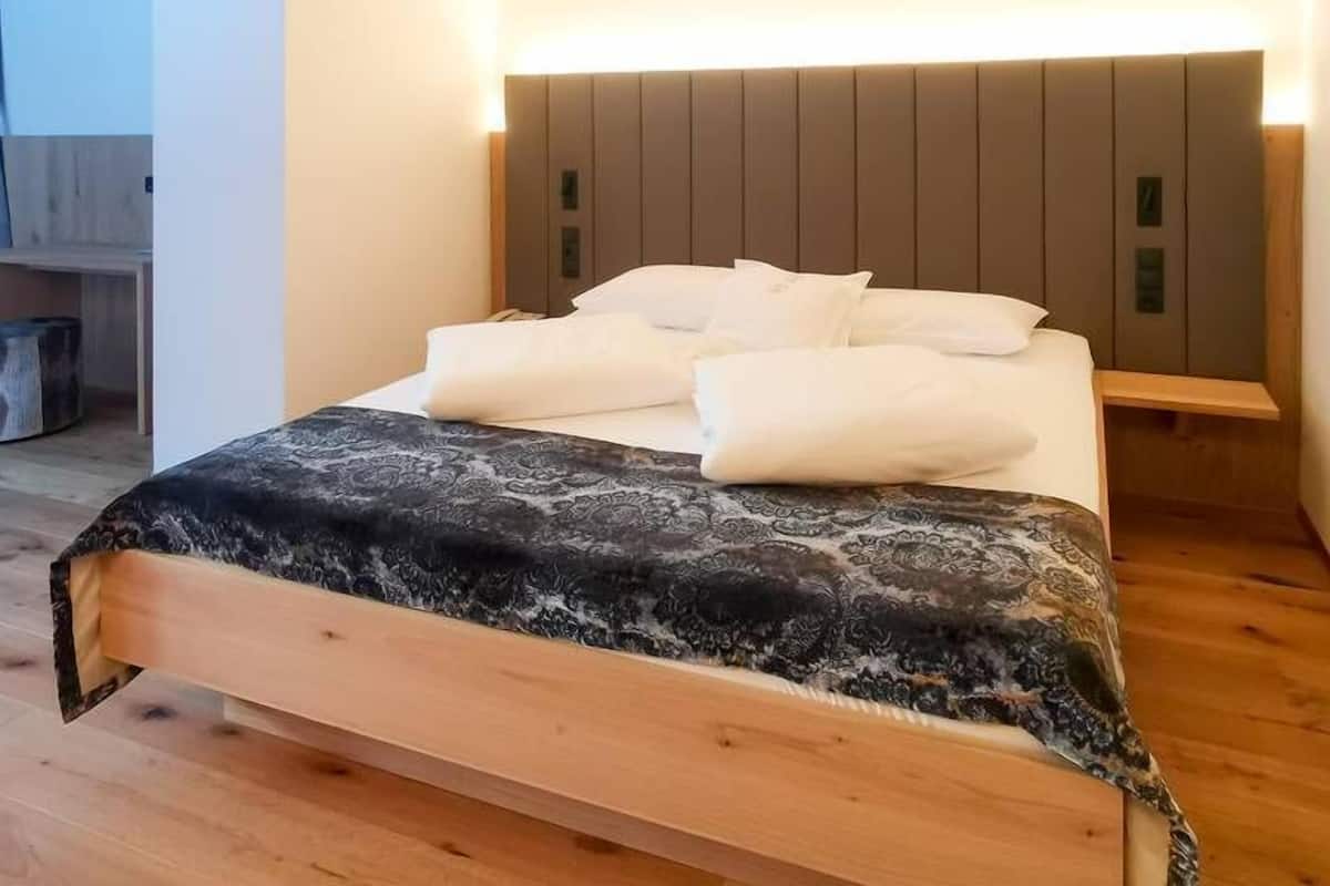 A neatly made bed with a patterned bedspread, a bedside table, and a headboard with built-in lighting.