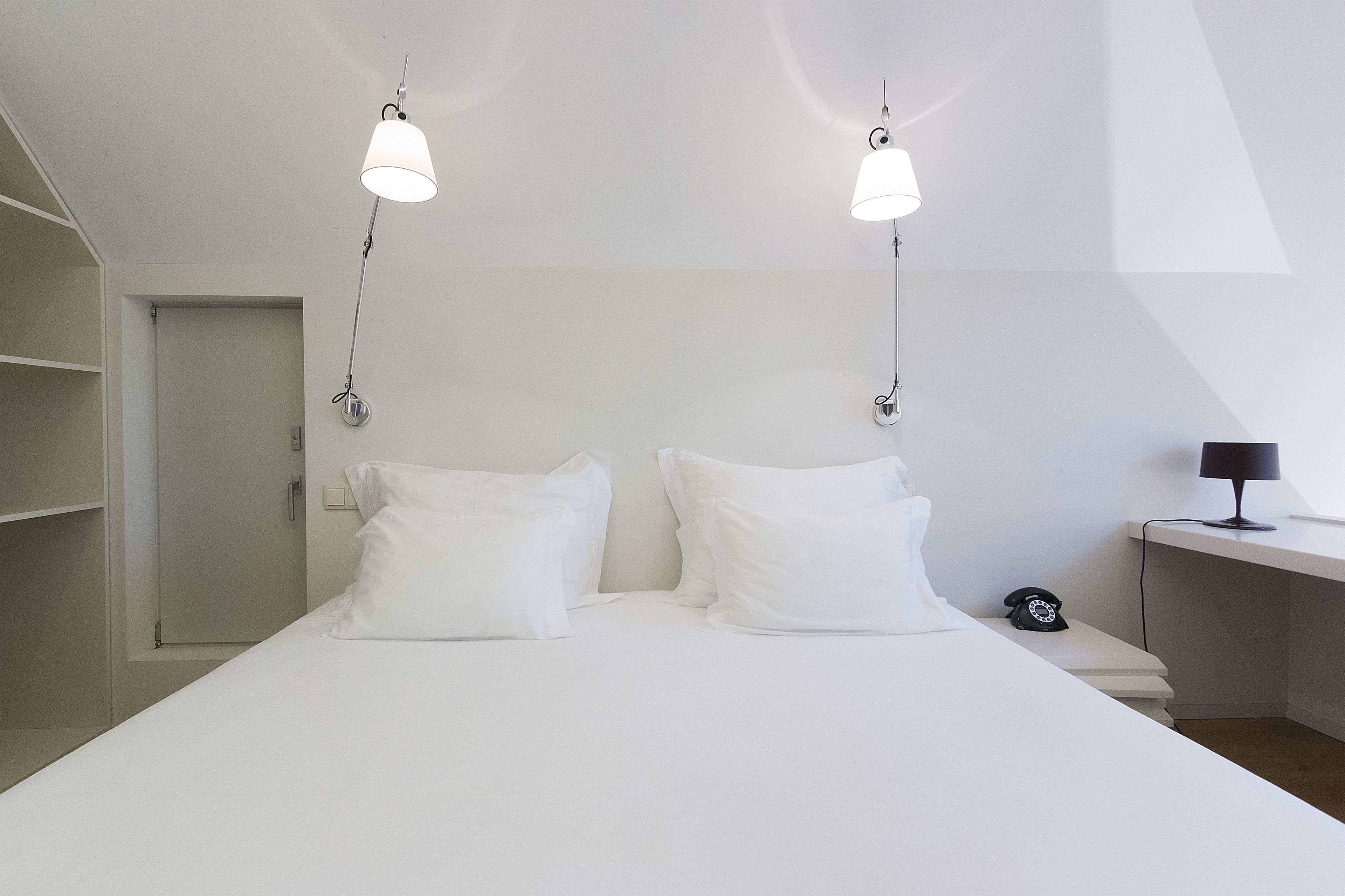 Un dormitorio moderno con una cama grande, dos lámparas de noche, un escritorio con lámpara y un teléfono.
