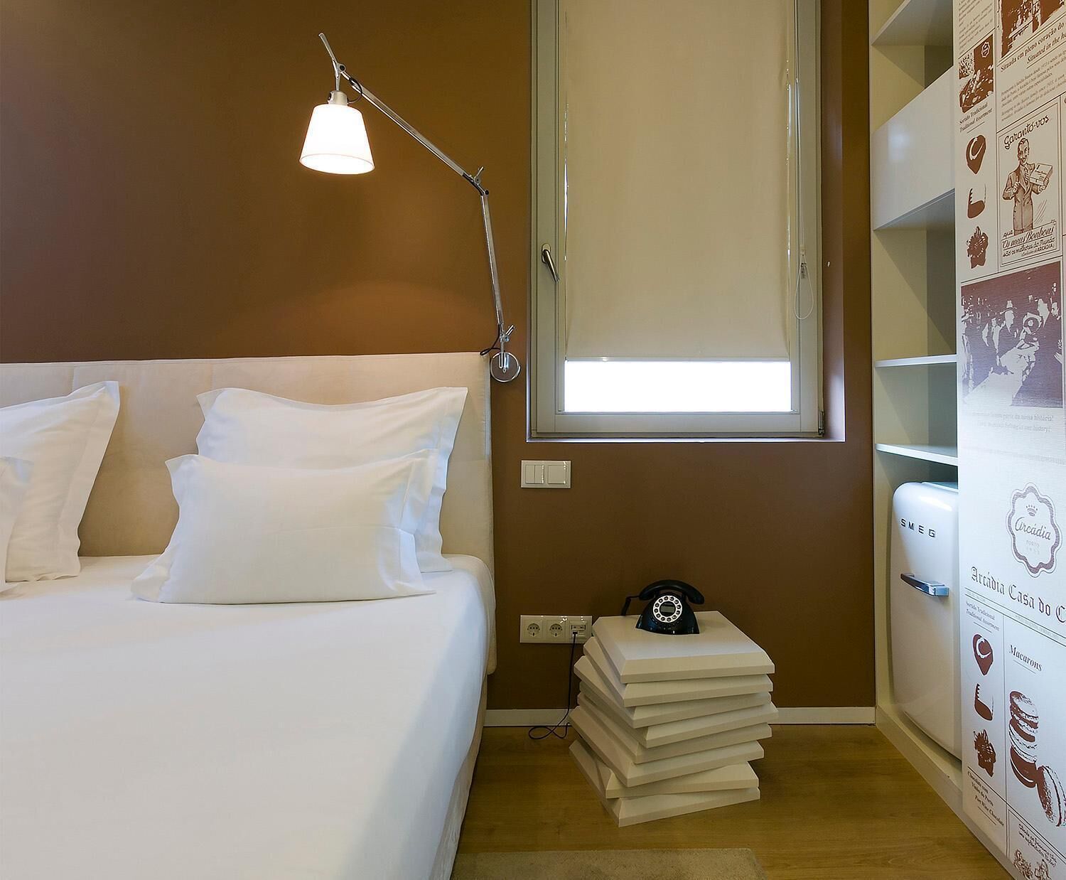A bedroom with a bed, a desk with a telephone, a window, and a wall with a poster.