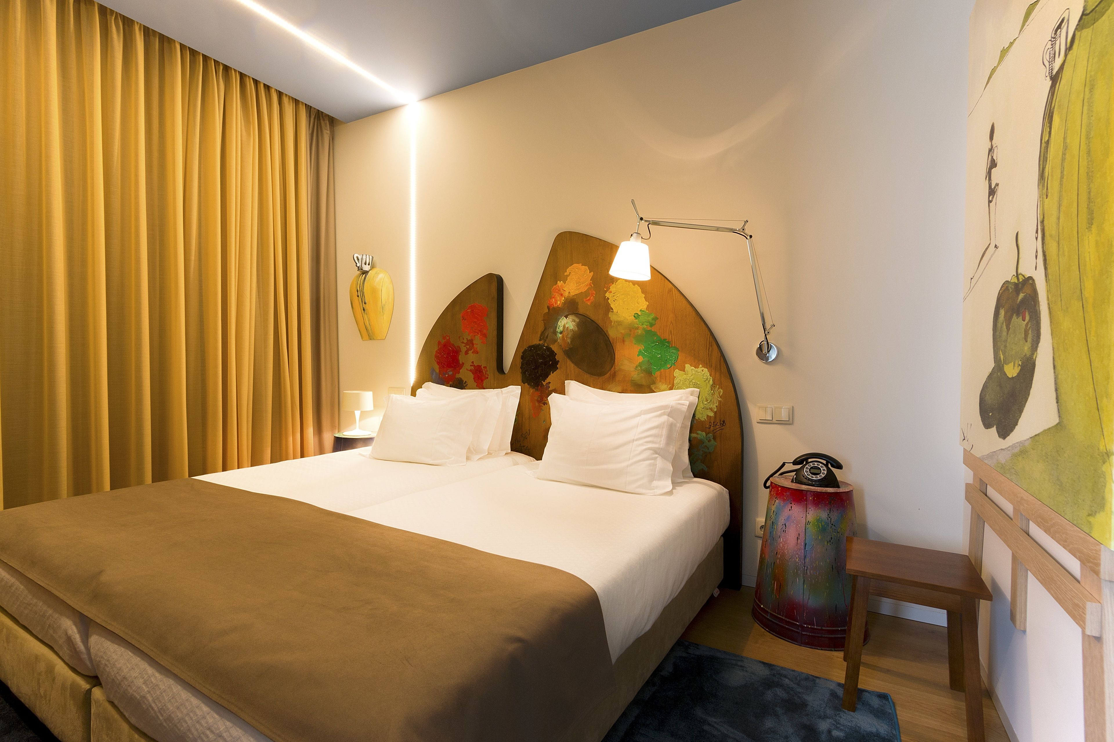 Une chambre d’hôtel avec un grand lit, une table de chevet, une lampe et un tableau coloré au mur.