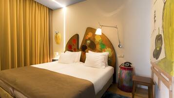 Une chambre d’hôtel avec un grand lit, une table de chevet, une lampe et un tableau coloré au mur.