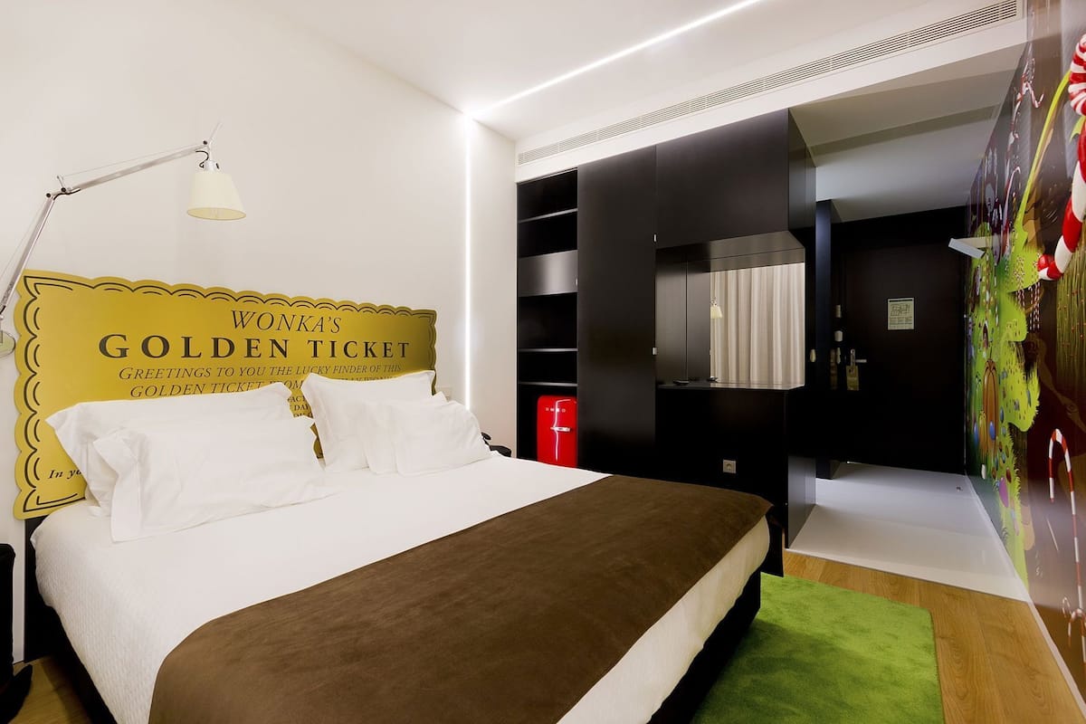 Ein Hotelzimmer mit Bett, Schreibtisch, Lampe, Kleiderschrank und Bad.