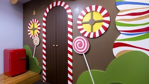 A room with a wooden door, striped wall decorations, and a red refrigerator.