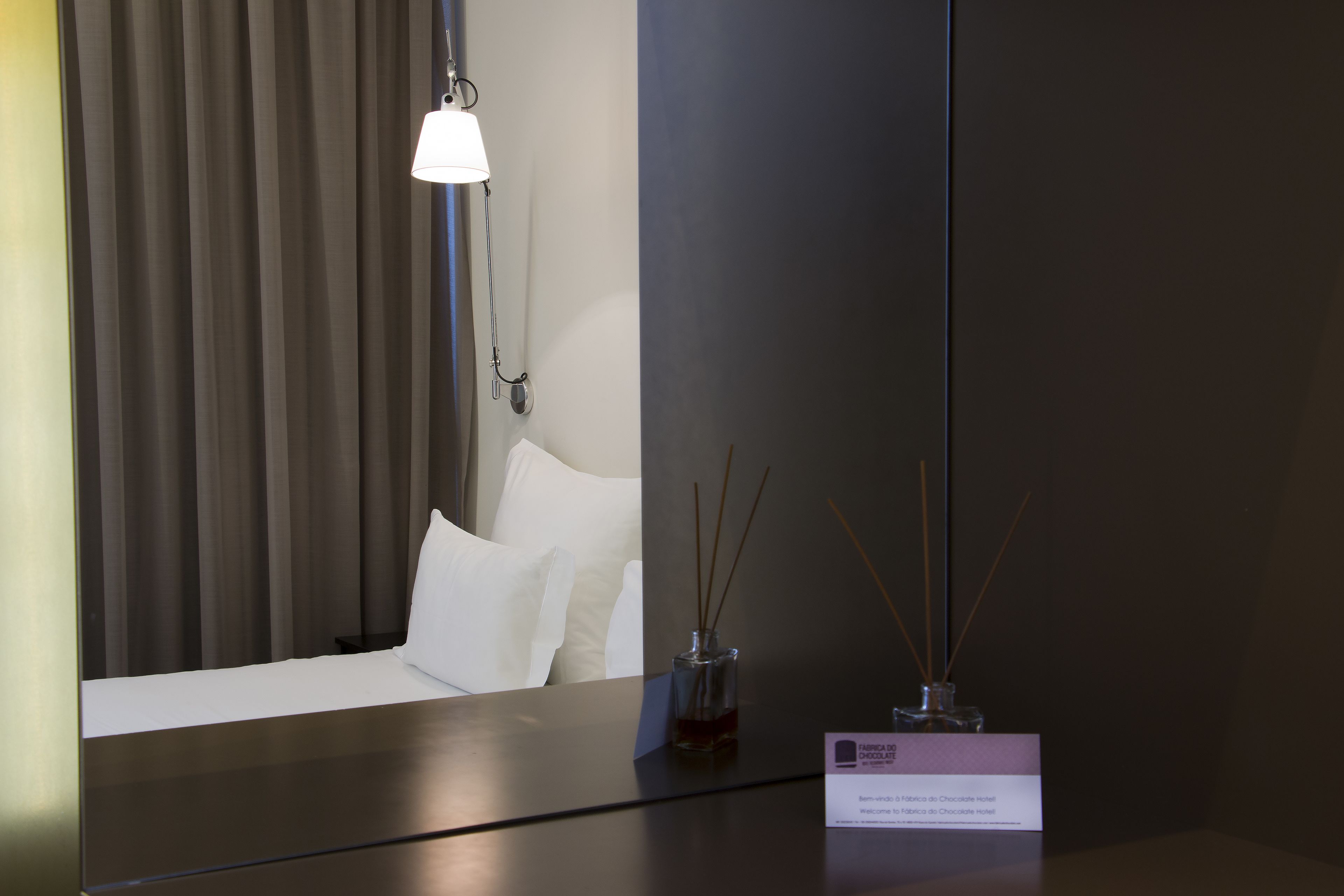 Ein Hotelzimmer mit einem Bett, einem Nachttisch mit Lampe, einer Vase mit Schilfrohrend und einem Schild mit Text.