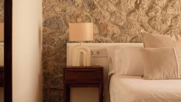 A bedroom with a stone wall, a bedside table with a lamp, and a bed with pillows.