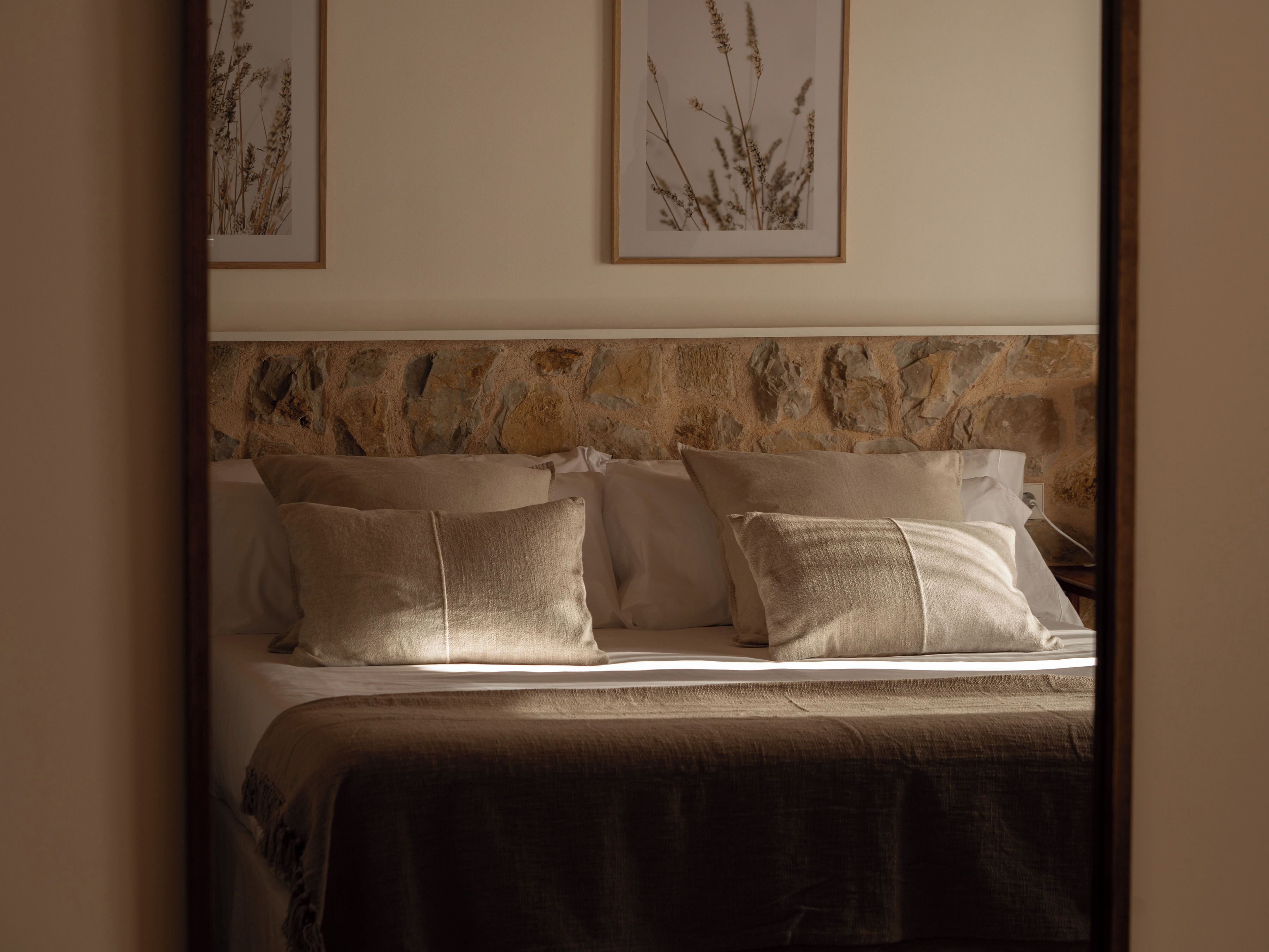 A bed with a stone headboard, multiple pillows, and a dark brown bedspread.
