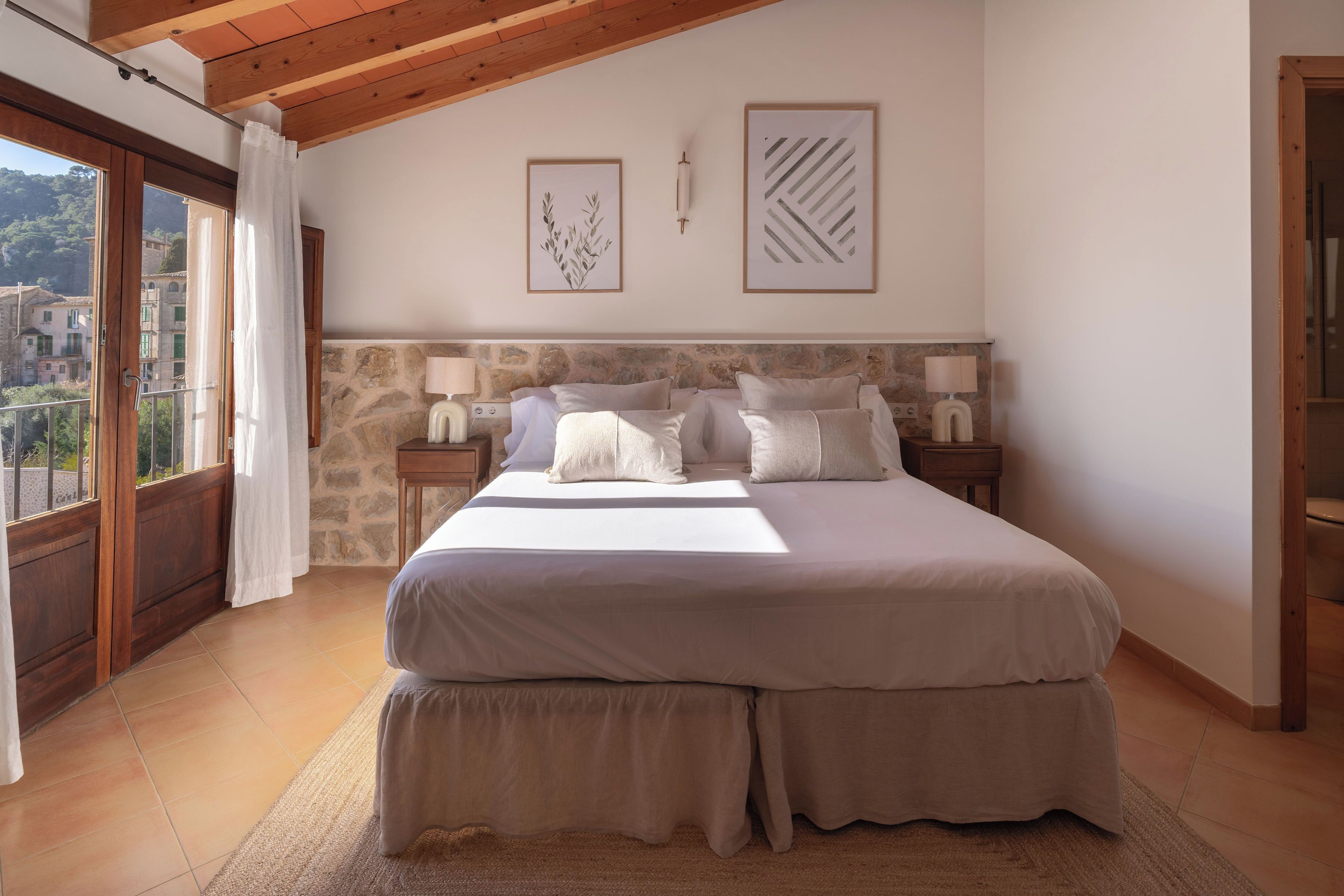 A bedroom with a large bed, stone headboard, two bedside tables with lamps, and framed artwork on the wall.