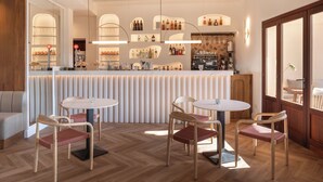 Eine Bar mit Holzbalkendecke, einer Theke mit Regalen voller Flaschen und vier runden Tischen mit Stühlen.