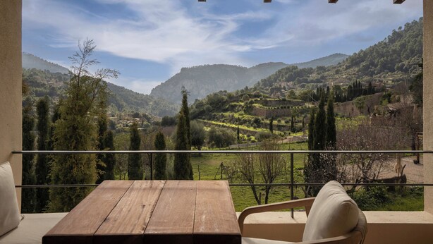 Ein Balkon mit einem Holztisch und Stühlen, der auf eine gebirgige Landschaft mit Terrassenfeldern und ein Dorf blickt.