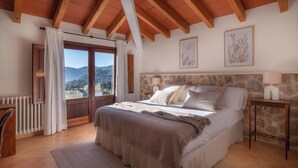 Ein Schlafzimmer mit einem großen Bett, Holzbalken, einer Steinwand und Blick auf die Berge.