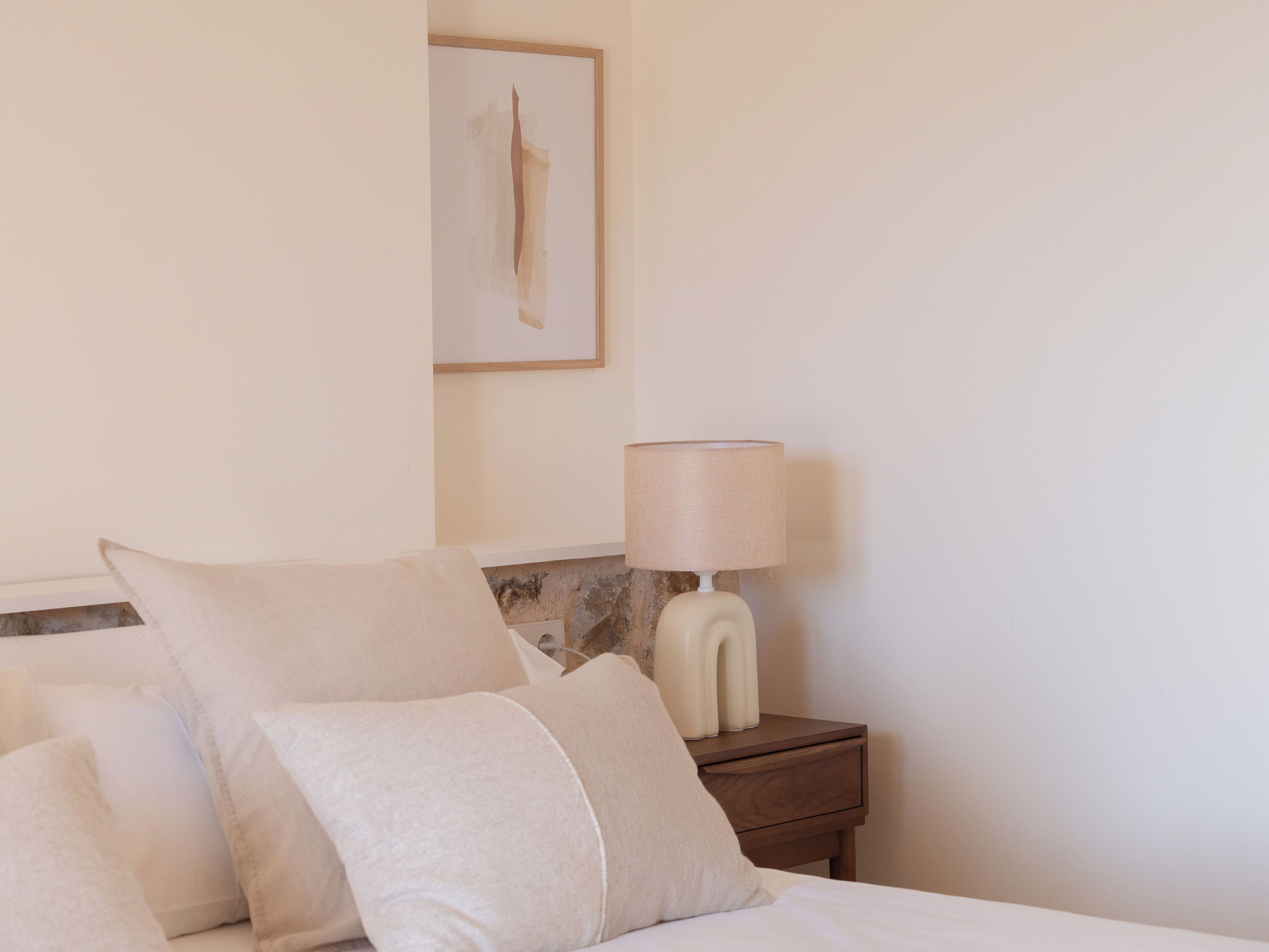 A neatly made bed with two pillows and a bedside table with a lamp.