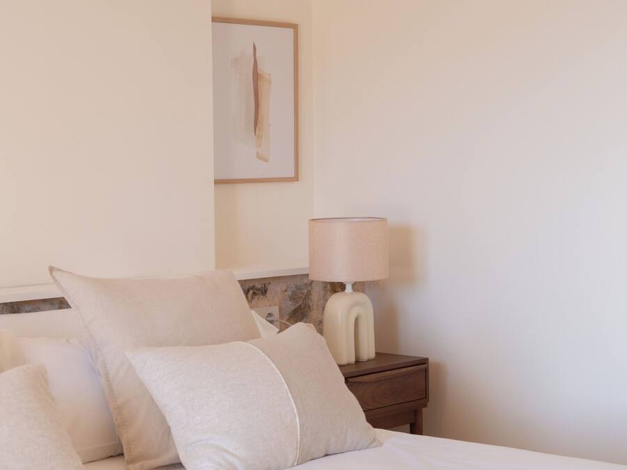 A neatly made bed with two pillows and a bedside table with a lamp.