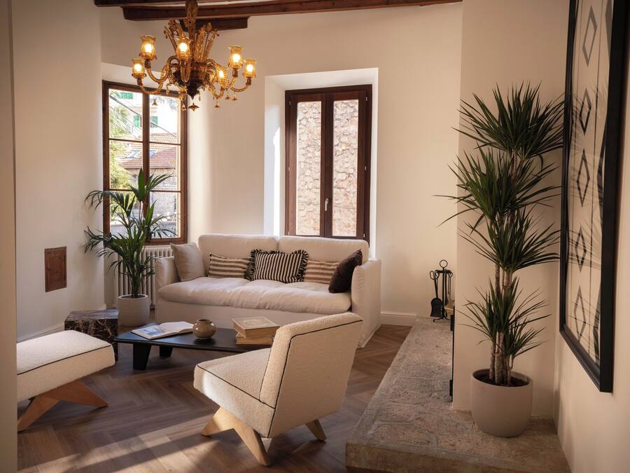 A living room with a sofa, armchair, coffee table, and potted plants.