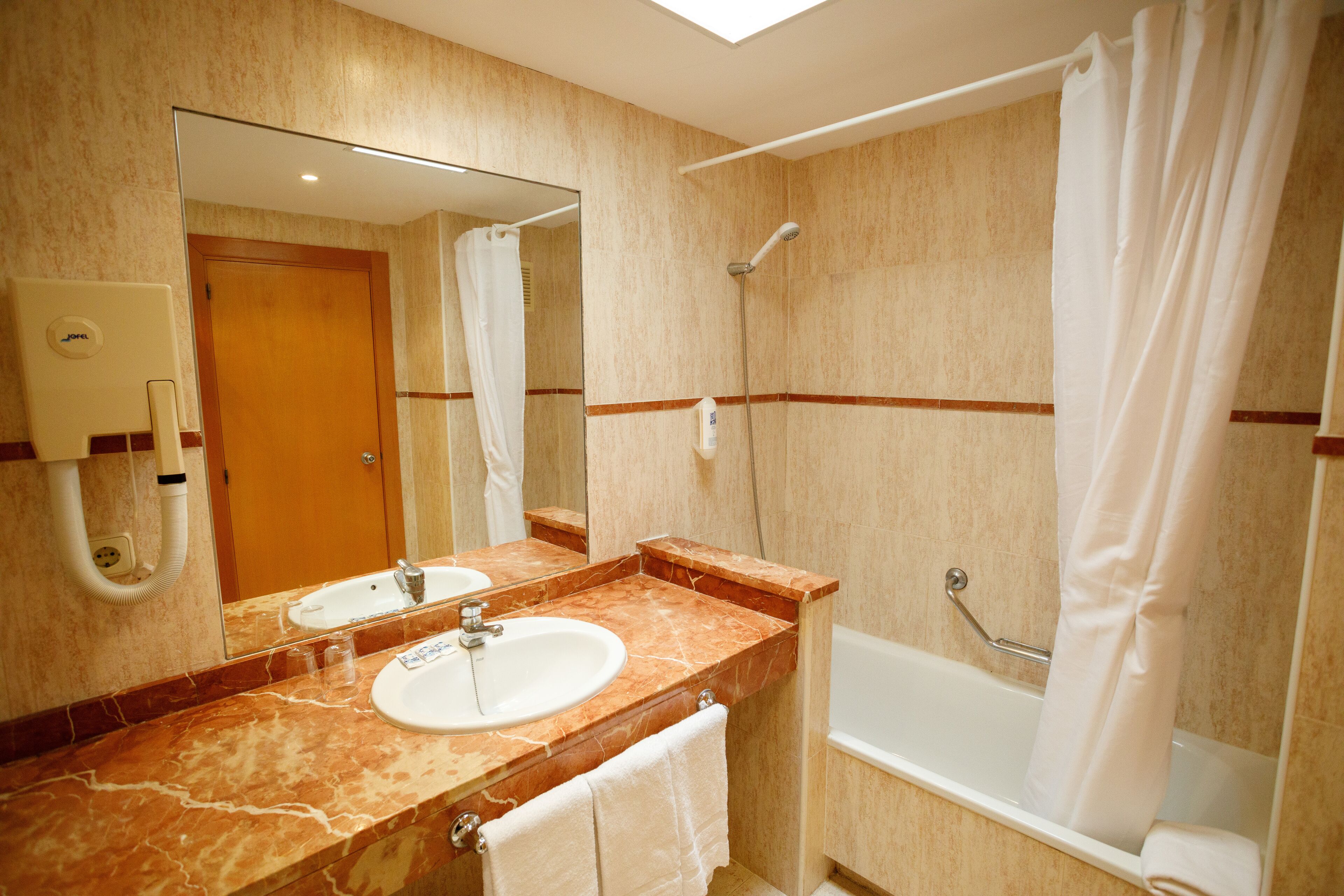 A bathroom with a sink, mirror, shower, and towel rack.