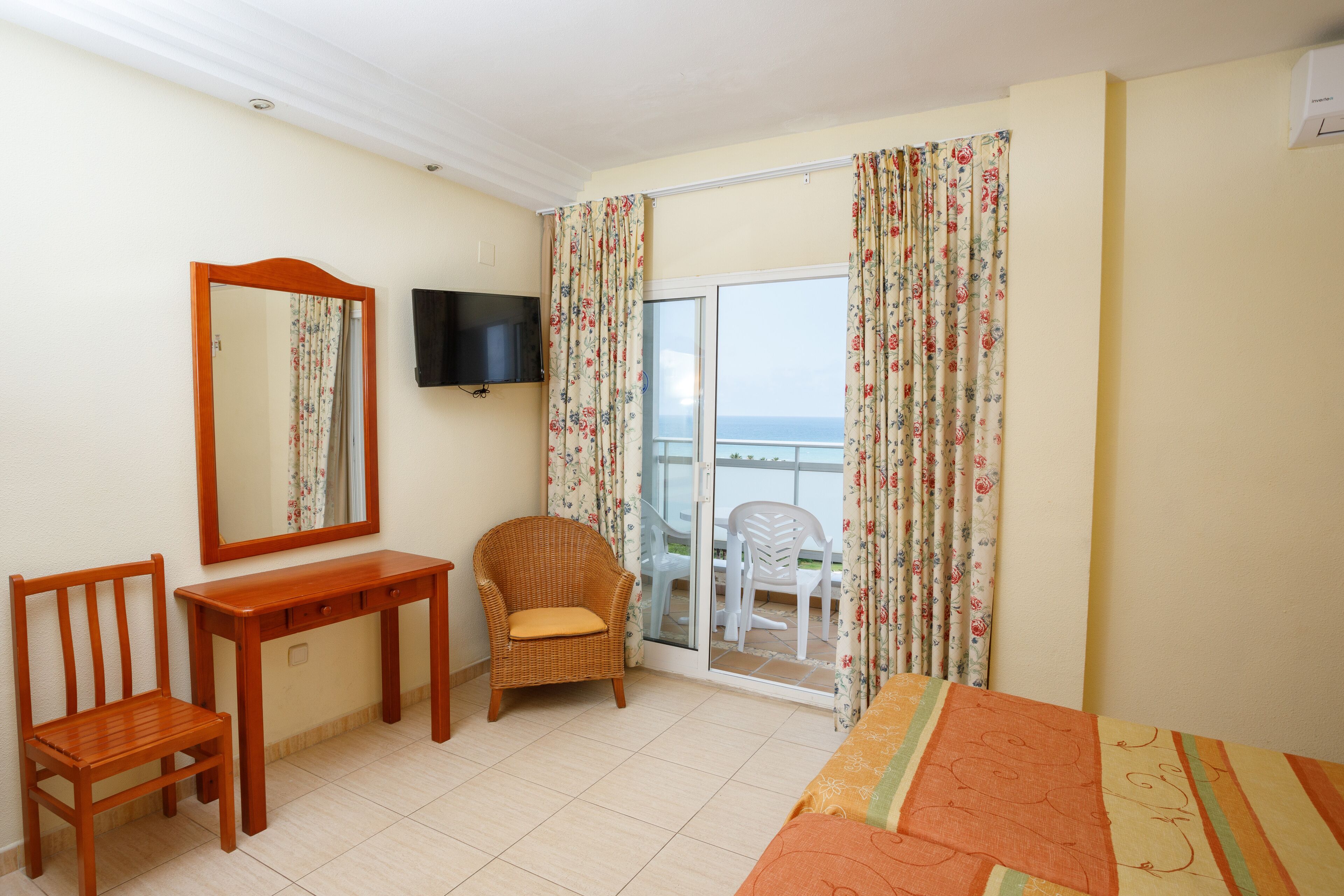 Habitación de hotel con un escritorio de madera, una silla, una cama, televisión y un balcón con vistas.