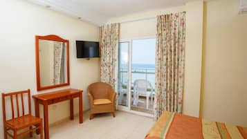 Habitación de hotel con un escritorio de madera, una silla, una cama, televisión y un balcón con vistas.