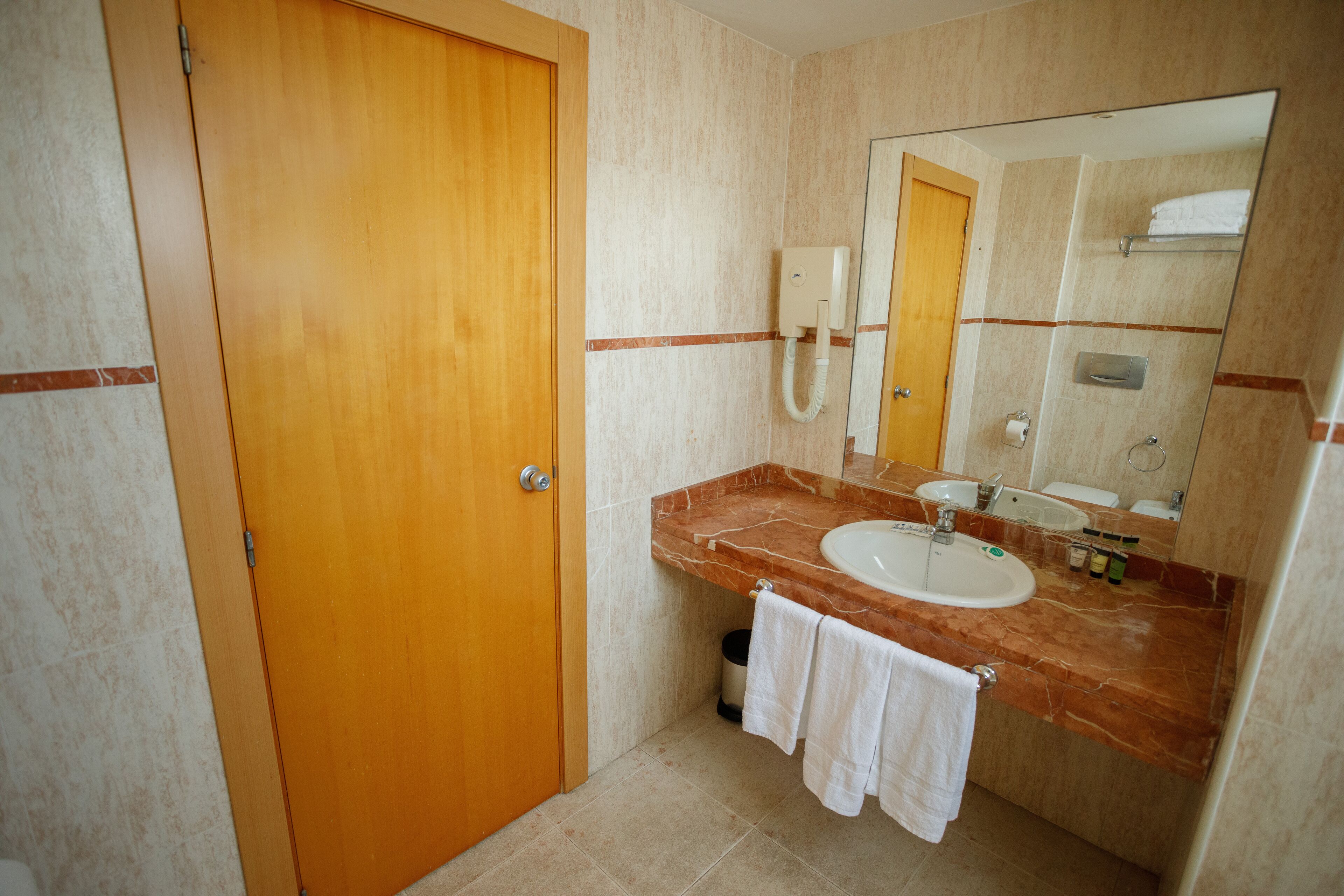 Un baño con puerta de madera, lavamanos de mármol, un espejo y un perchero para toallas.