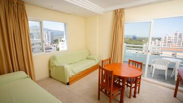 Una habitación de hotel con balcón, un sofá, una mesa de comedor y sillas.
