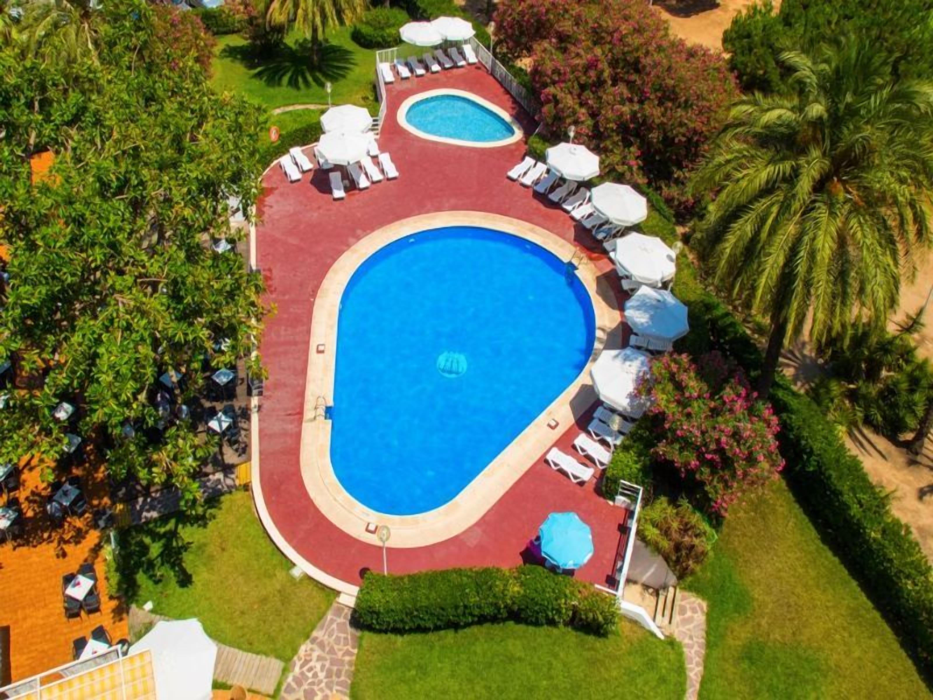 Una piscina ovalada grande con borde rojo, rodeada de sillones y sombrillas.