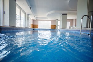 Una piscina techada, una piscina al aire libre, sombrillas