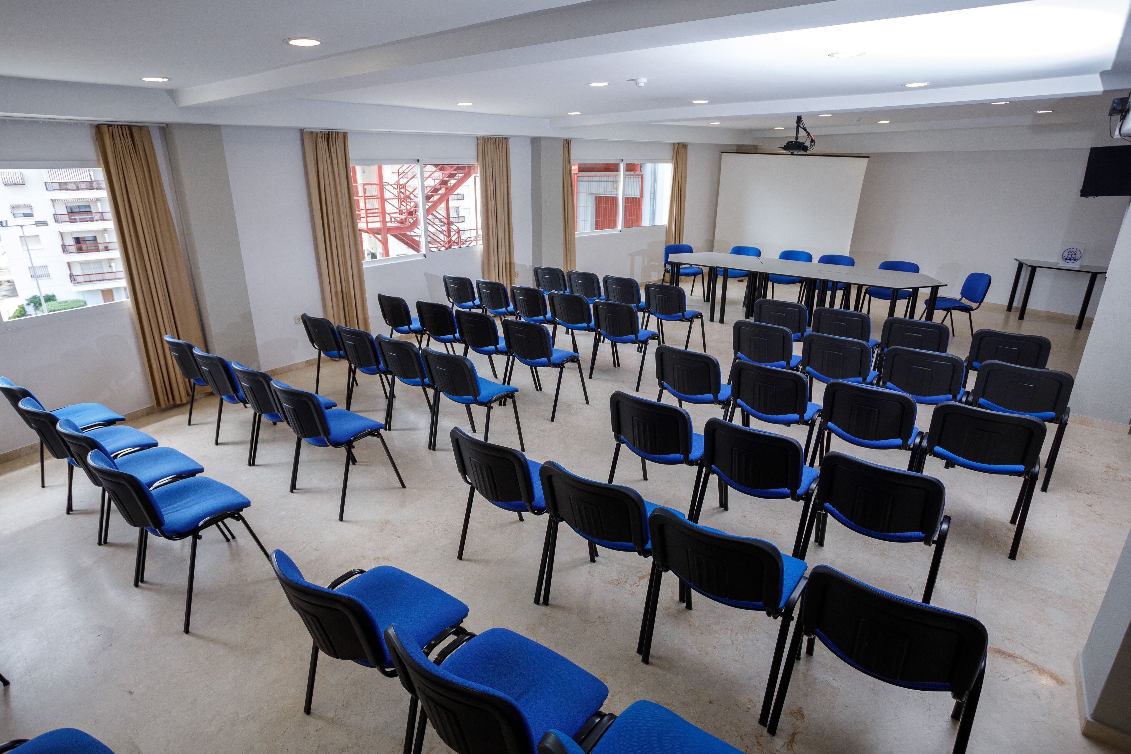 Uma sala de conferências com fileiras de cadeiras azuis, um quadro branco e uma tela de projetor.