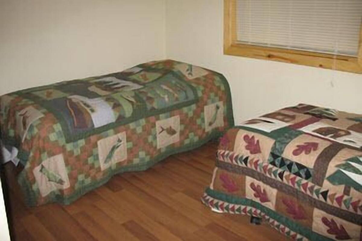 Una habitación con dos camas cubiertas con colchas estampadas, suelo de madera y una ventana con persianas.