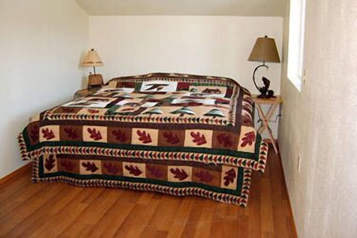 Un dormitorio con cama, mesita de noche, lámpara y ventana.