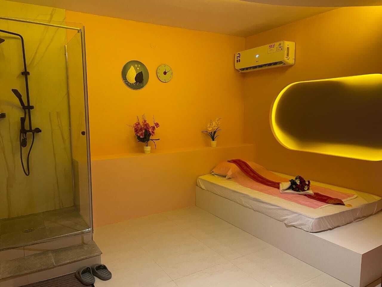 Une chambre avec une douche à parois de verre, un lit recouvert d’une couverture rouge et deux horloges fixées au mur.