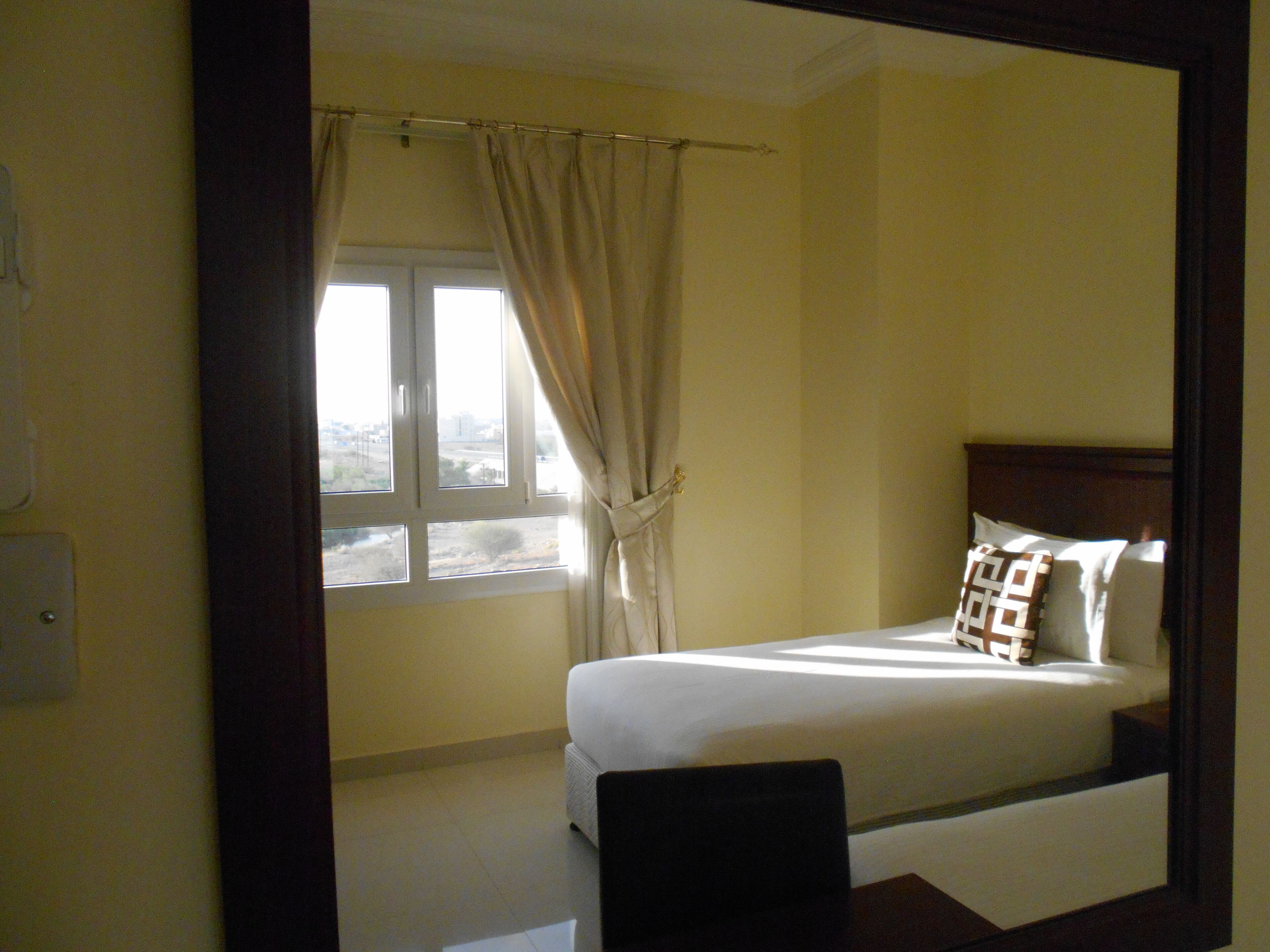 A hotel room with a bed, a window with curtains, and a view of the outside.