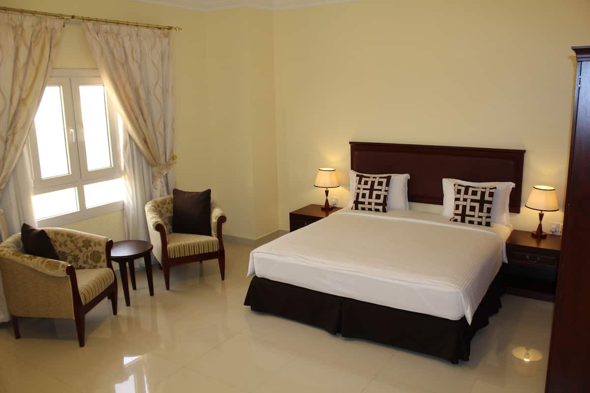 A hotel room with a large bed, two bedside tables with lamps, a chair, and a window with curtains.
